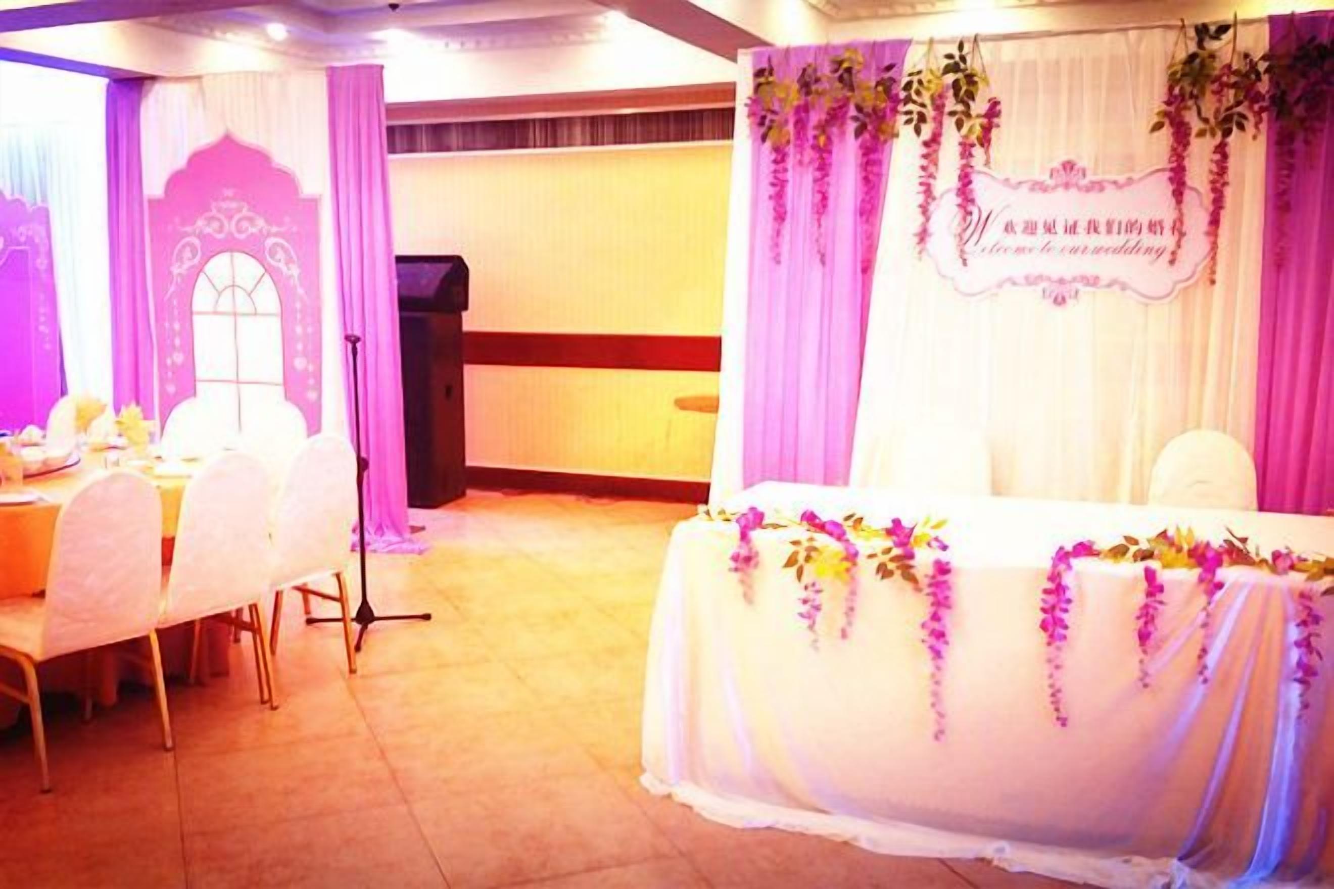 A banquet hall with a long table set for a meal, a stage with a backdrop, and a decorative archway.