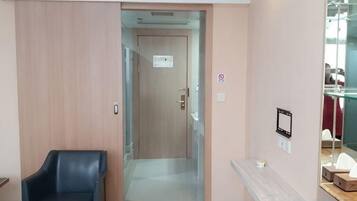 A hotel lobby with a wooden door, a black chair, a marble bench, and a glass display case.