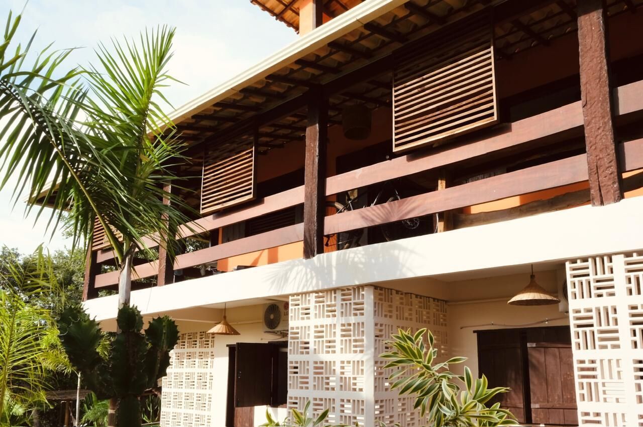 A multi-story building with wooden balconies, white lattice screens, and a palm tree in the foreground.