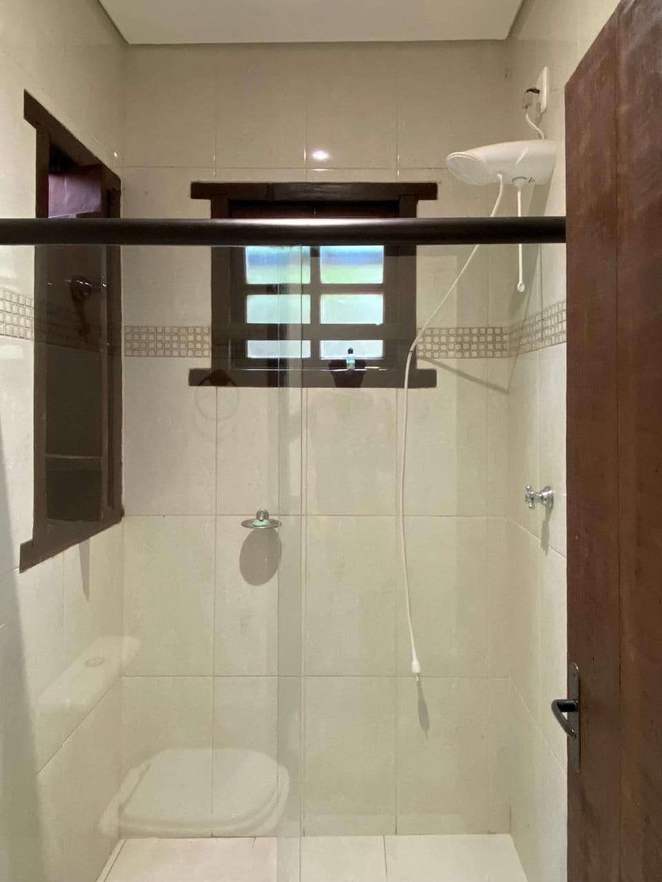 A small, enclosed shower area with a glass door, a toilet, and a window above the shower.