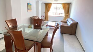 A modern living room with a glass dining table, leather sofas, and a large window with curtains. - GRAN HOTEL CALI  (Cali)