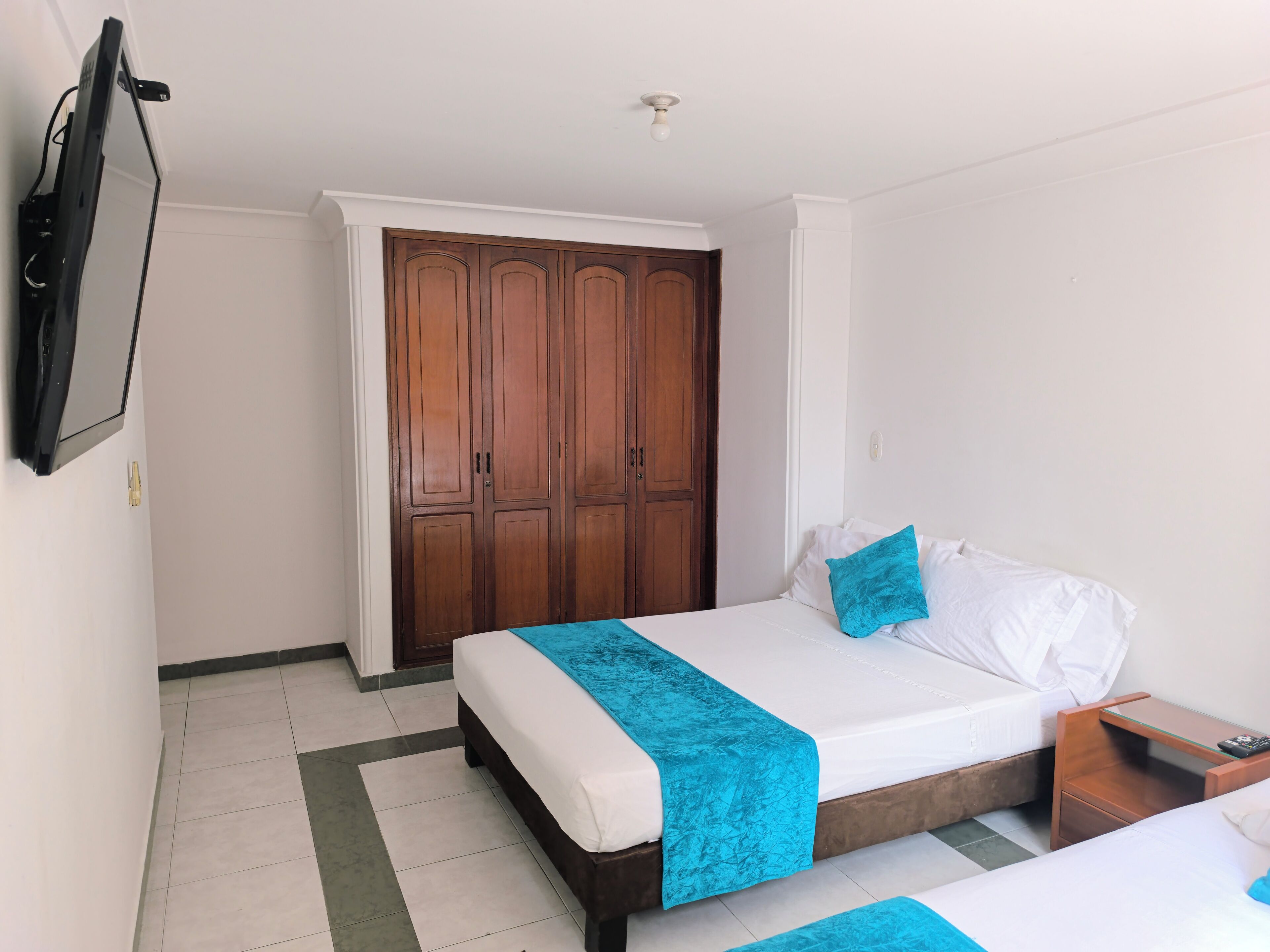 Una habitación de hotel con una cama, un armario de madera, un televisor y una mesita de noche.