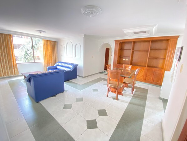A spacious room with a blue sofa, a glass-top dining table with chairs, and a wooden cabinet. - GRAN HOTEL CALI (Cali)