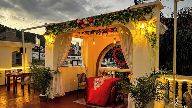 A cozy outdoor seating area with a red canopy, potted plants, and a view of the cityscape. - GRAN HOTEL CALI  (Cali)