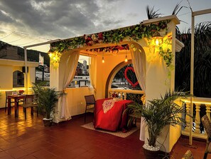 A cozy outdoor seating area with a red canopy, potted plants, and a view of the cityscape. - GRAN HOTEL CALI  (Cali)