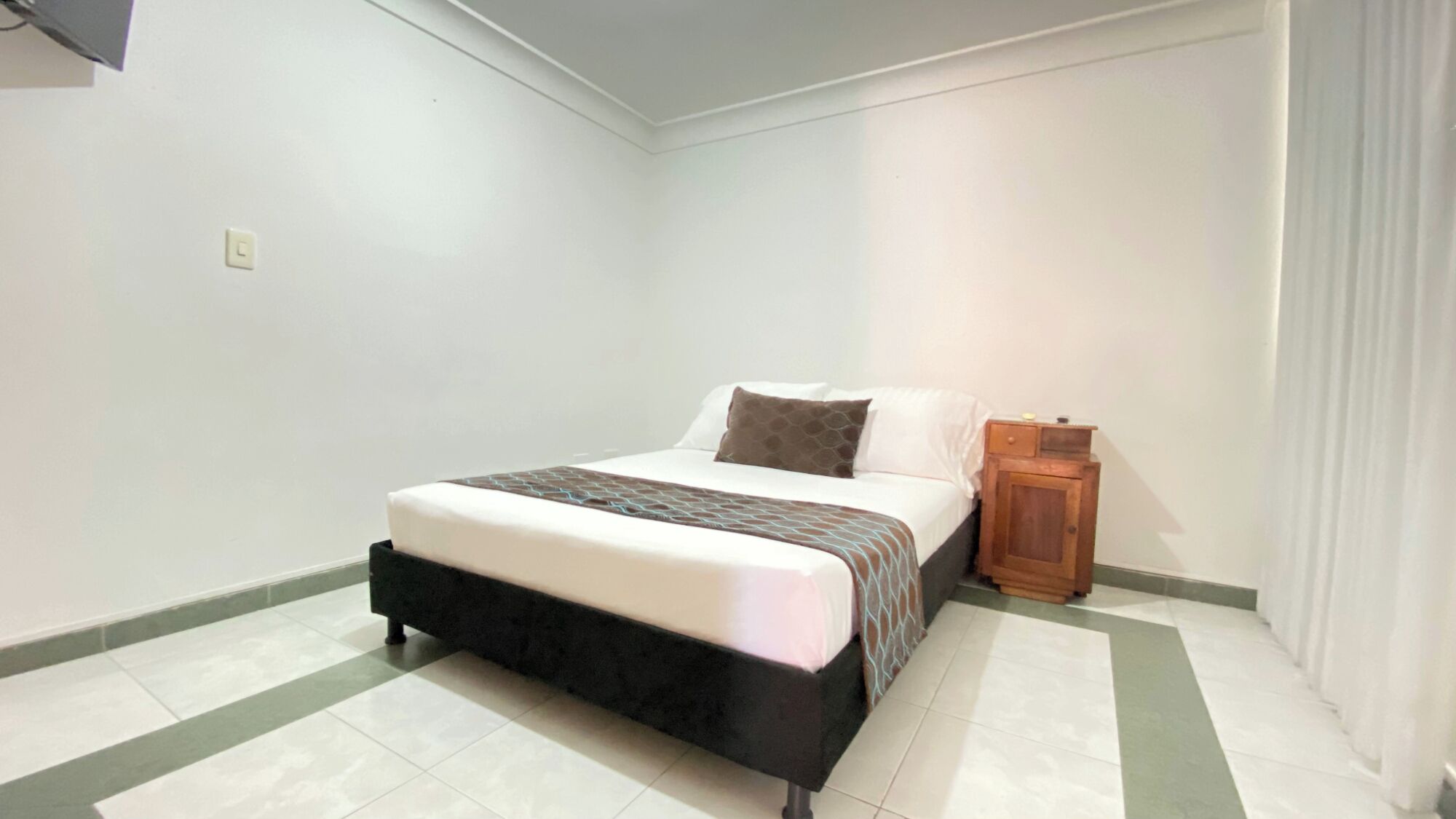 A bedroom with a bed, a nightstand, and a wall-mounted TV.