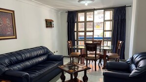 A living room with a dark blue leather sofa, a glass coffee table, and a dining table with chairs. - GRAN HOTEL CALI  (Cali)