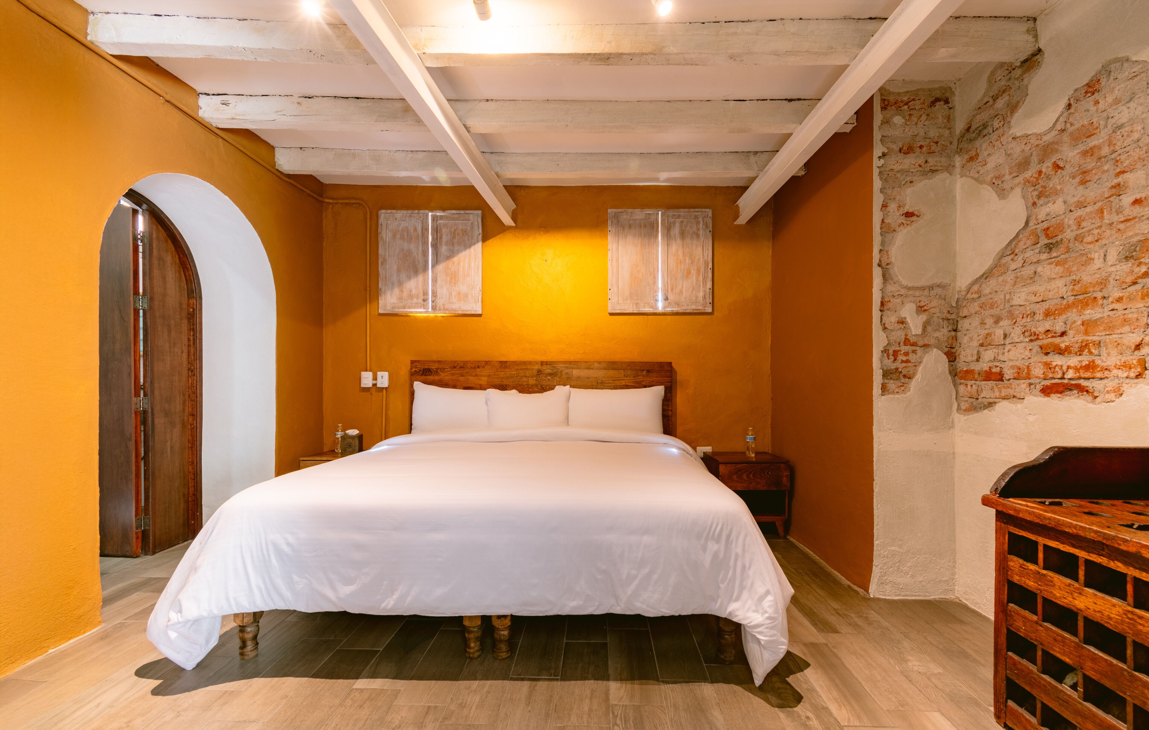 Ein Schlafzimmer mit einem hölzernen Kopfteil, einem großen Bett, einer Holzbank und einer Ziegelwand.