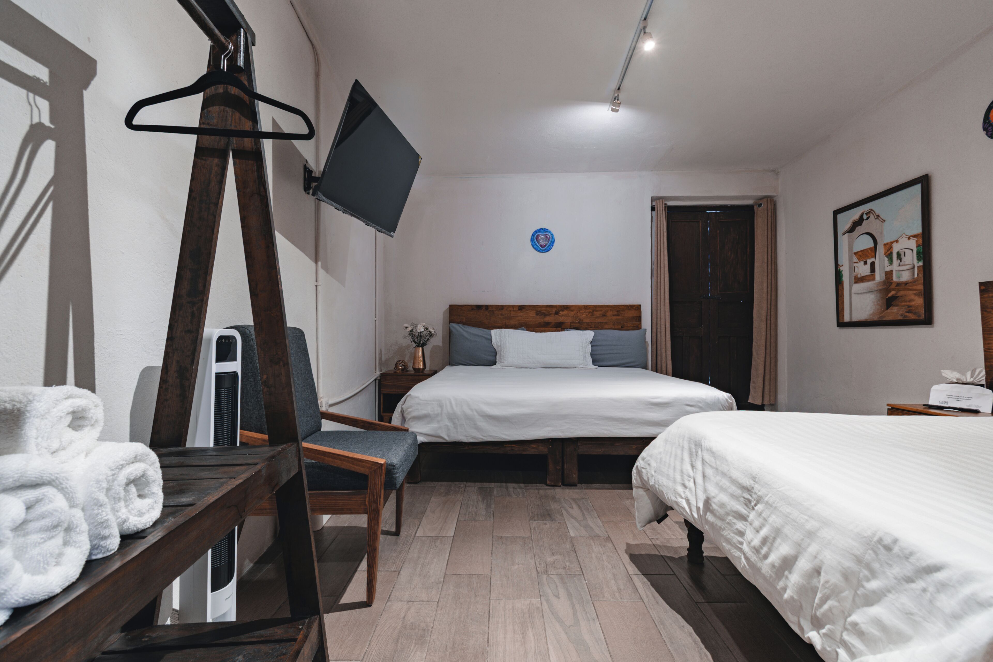 A hotel room with two beds, a TV, a wooden chair, and a desk with towels.