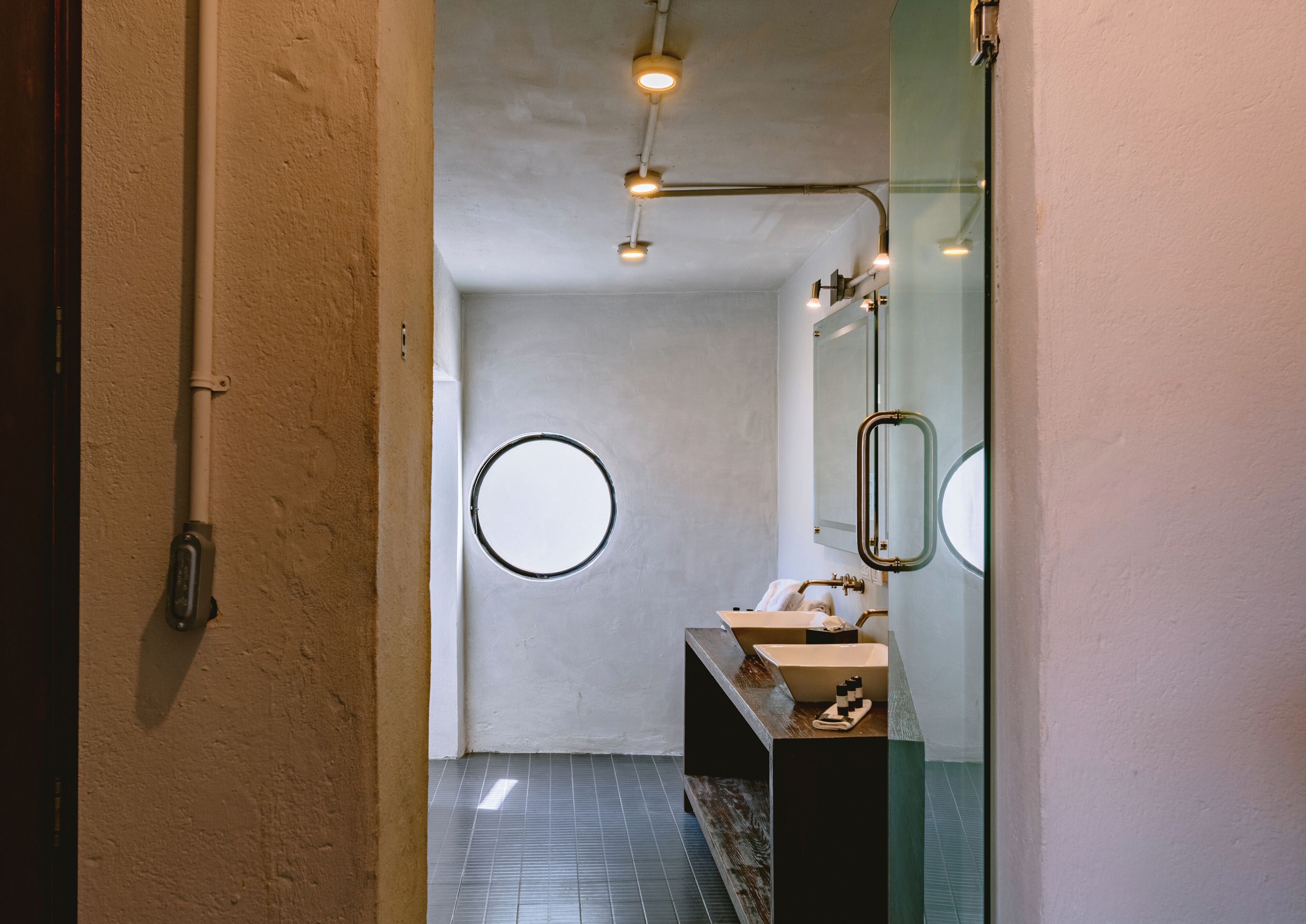 A modern bathroom with a round mirror, two sinks, and a shower.