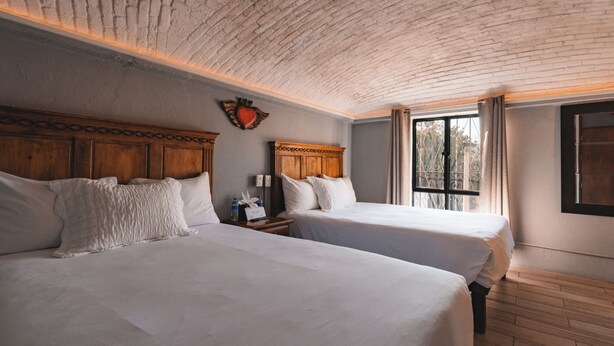 A room with two beds, wooden headboards, a brick ceiling, and a window with curtains. - Casa Xaca (San Miguel de Allende)