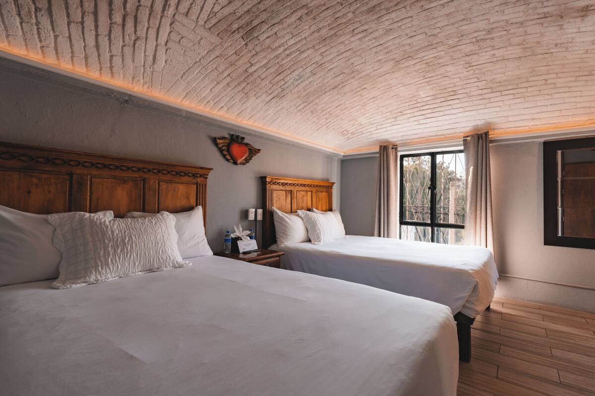 Een kamer met twee bedden, houten hoofdborden, een bakstenen plafond en een raam met gordijnen.