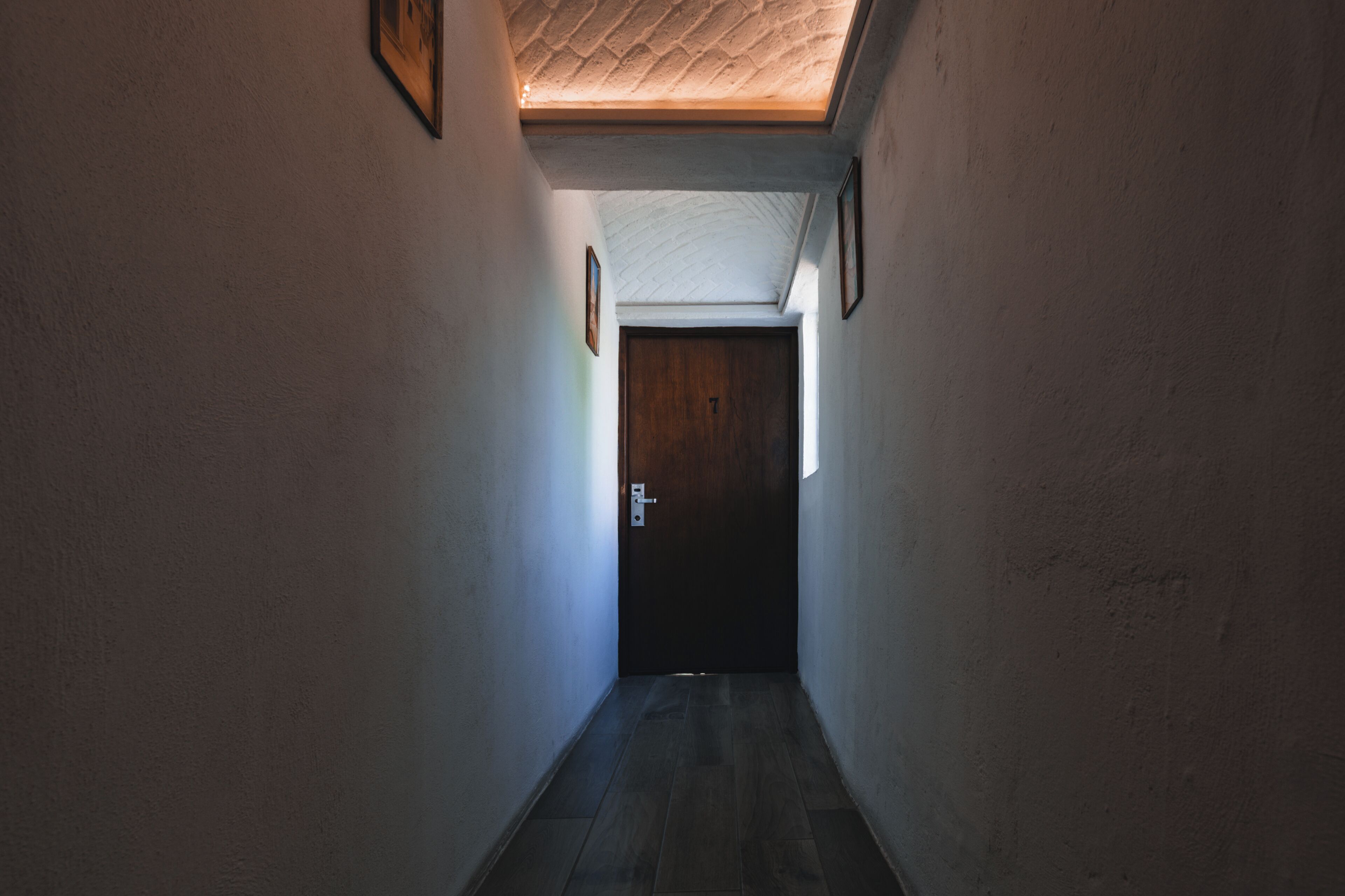 Un pasillo estrecho con una puerta de madera al final, paredes blancas y techo con textura.