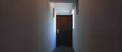 Un pasillo estrecho con una puerta de madera al final, paredes blancas y techo con textura.
