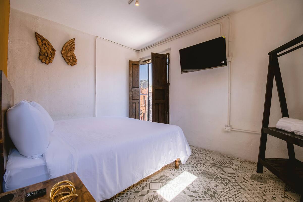 Een slaapkamer met een bed, een aan de muur bevestigde televisie en een houten plank.