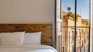 A bedroom with a wooden headboard, a bed with white bedding, and a view of a balcony with a railing and buildings in the background. - Casa Xaca (San Miguel de Allende)