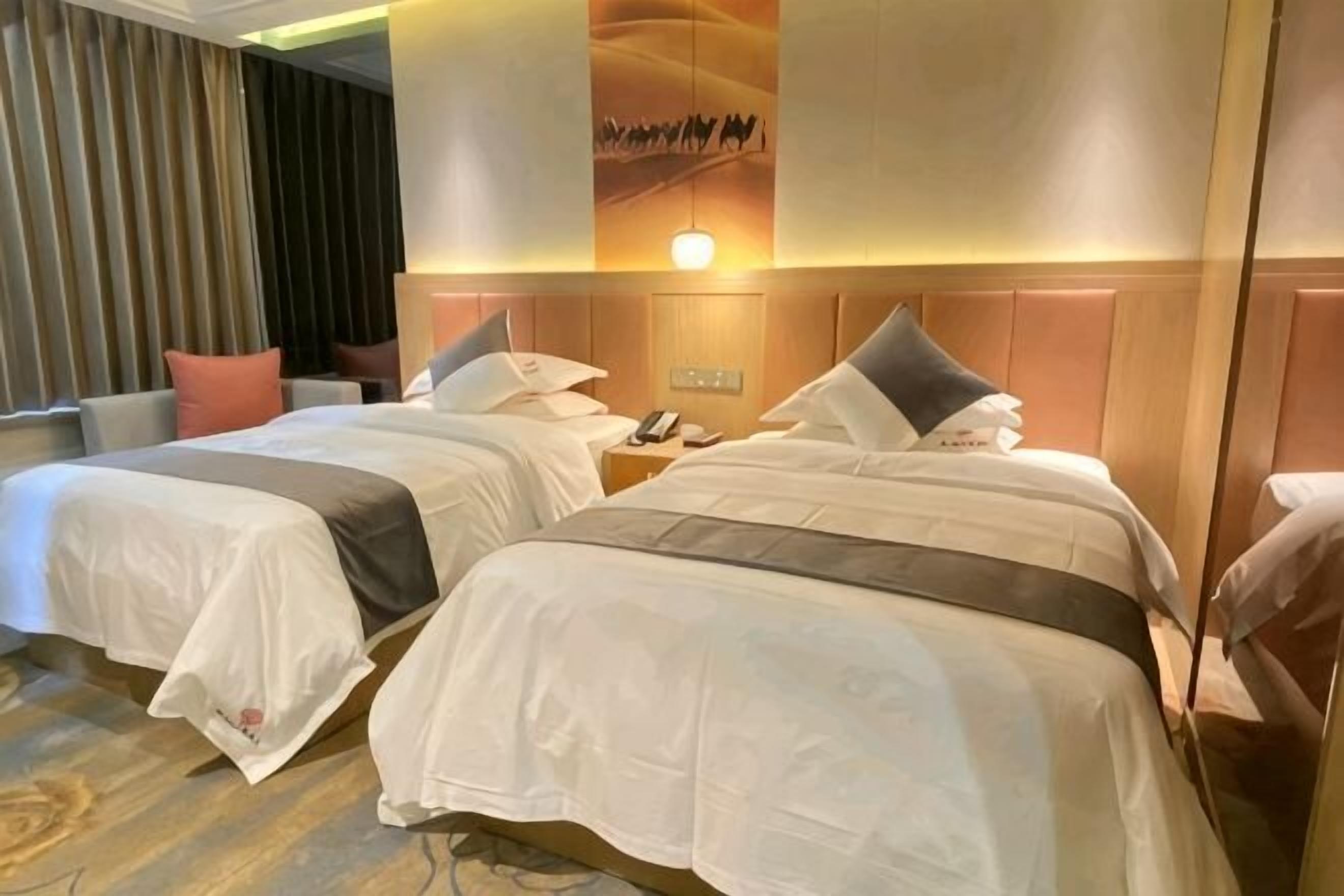 A hotel room with two beds, a nightstand with a phone, and a wall-mounted light.