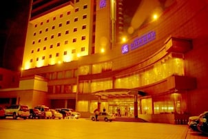 Un hotel con una estructura de varios pisos, un acceso cubierto y un área de estacionamiento con varios automóviles.
