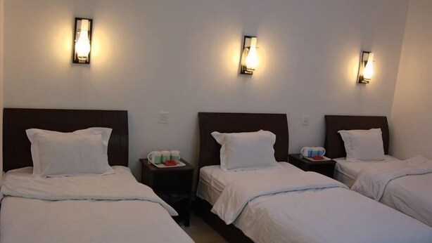 A hotel room with three single beds, each with a headboard and white bedding. There are bedside tables with lamps and a tray with cups and a red object. - Anxin Huaxin Hotel (Anxin)