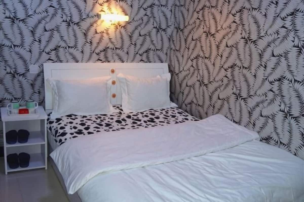 A neatly made bed with a white headboard, a bedside table with a lamp, and a patterned wallpaper.