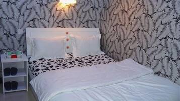A neatly made bed with a white headboard, a bedside table with a lamp, and a patterned wallpaper.