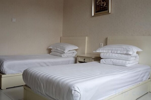 Dos camas individuales con ropa de cama blanca, una mesita de noche con lámpara y un cuadro en la pared.