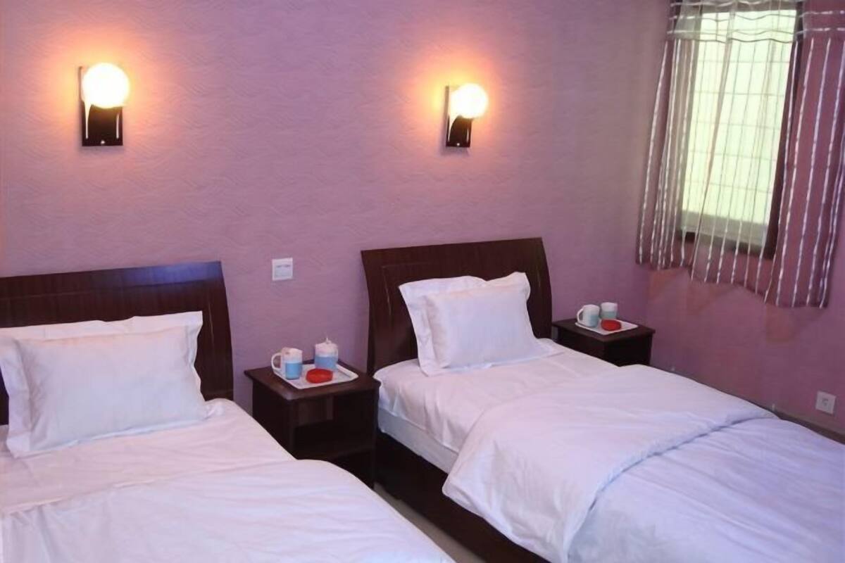 A hotel room with two beds, nightstands, wall sconces, and a window with curtains.