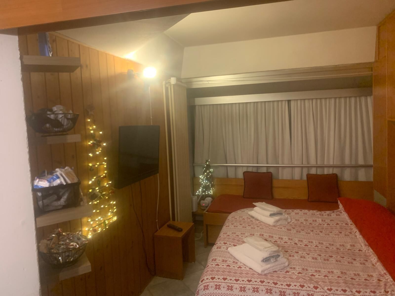 Une chambre d’hôtel avec un lit, une télévision, un sapin de Noël et une fenêtre avec des rideaux.