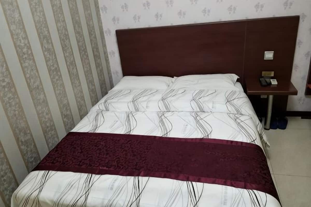 A bed with a patterned bedspread and a dark red blanket, a wooden headboard, a bedside table with a phone, and a wall with striped wallpaper.