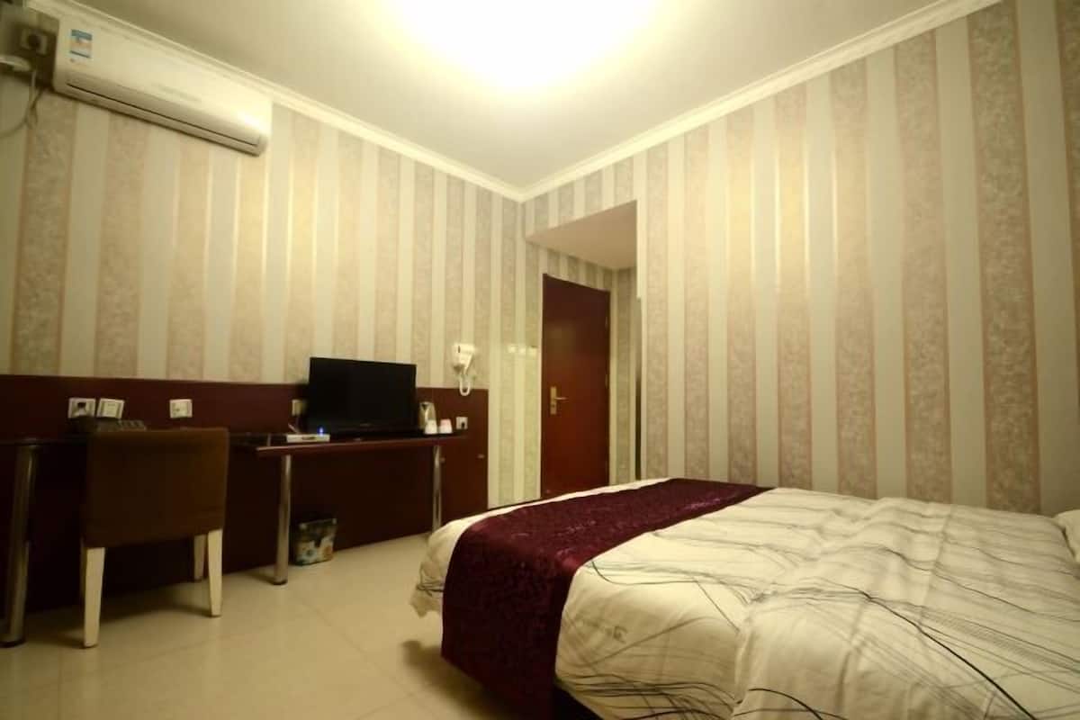 A hotel room with a bed, a desk, a chair, a television, and an air conditioning unit.