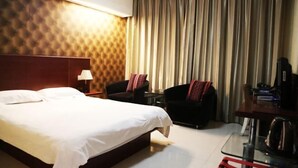 Quarto de hotel com uma cama grande, uma escrivaninha com chaleira, uma cadeira e uma televisão.