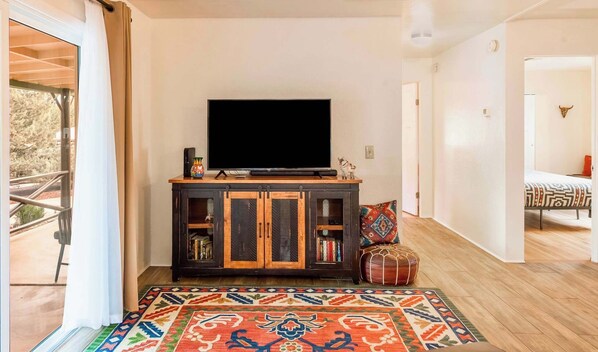 A living room with a television on a wooden cabinet, a colorful rug, and a door leading to another room.