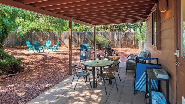 A covered patio with a table and chairs, a grill, and a wooden fence in the background.