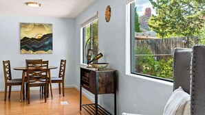 A dining area with a table and chairs, a decorative bowl on a stand, and a painting on the wall.