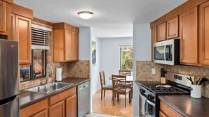 A modern kitchen with wooden cabinets, stainless steel appliances, and a dining area with wooden chairs.