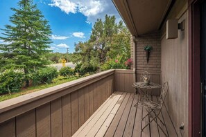 Eine Holzterrasse mit einem Metalltisch und Stühlen, mit Blick auf eine Straße mit Warnschild und Bäumen.