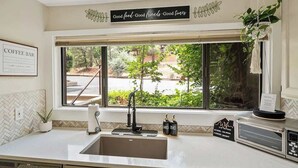 Una cocina con un ventanal grande, un lavamanos, un letrero de cafetería y un cartel que dice "Good food, Good friends, Good times".