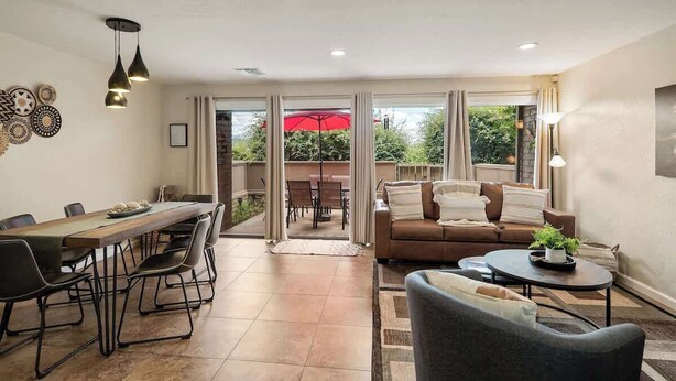 Una sala de estar moderna con comedor, sofá y mesa de centro. Hay una puerta corrediza de vidrio que da a un patio exterior con una sombrilla roja.