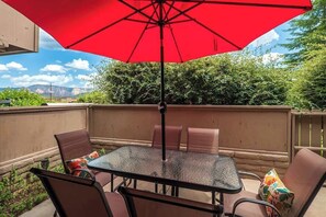 Eine Terrasse mit einem Glastisch und Stühlen, einem roten Sonnenschirm und Blick auf Berge.