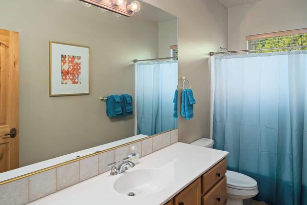 Un baño con un espejo grande, lavamanos, inodoro y cortina de ducha.
