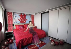 Une chambre d’hôtel avec un lit, une couvre-lit rouge, un grand élément de décoration murale rouge et un coussin à motifs rouges et blancs.