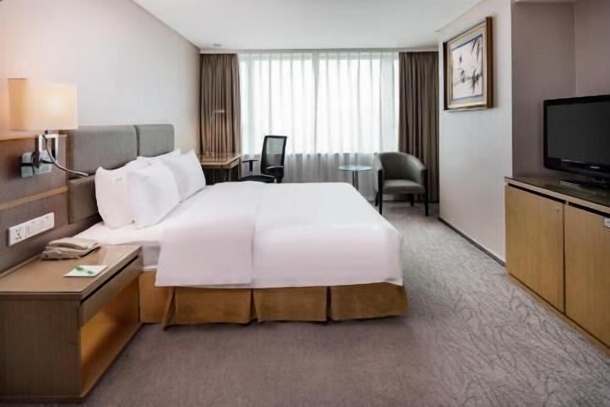 A hotel room with a bed, a desk, a chair, a television, and a window with curtains.