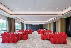Une salle de conférence avec des tables rondes et des chaises rouges, de grandes fenêtres et un tapis à motifs.