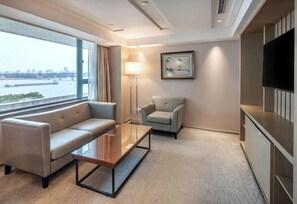 Une chambre d’hôtel avec un canapé, une table basse, une lampe, un téléviseur et une vue sur une rivière.