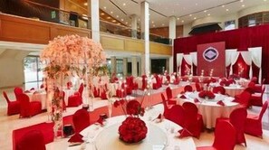 A banquet hall with round tables, red chairs, and floral centerpieces.