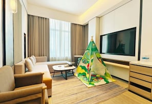 Une chambre d’hôtel moderne équipée d’un canapé, d’une télévision, d’une petite table et d’une tente de jeu aux couleurs vives.