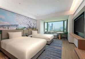 A hotel room with two beds, a TV, a desk, and a large window with a city view. - Holiday Inn WUHAN RIVERSIDE by IHG (Wuhan)