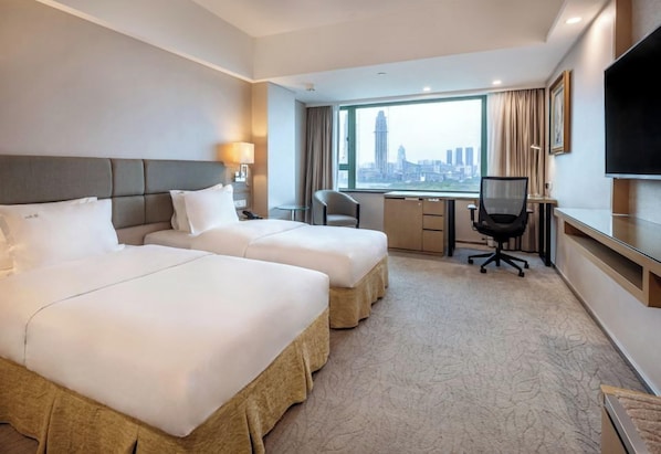 Une chambre d’hôtel avec deux lits, un bureau, une chaise, une télévision et une grande fenêtre donnant sur la ville.