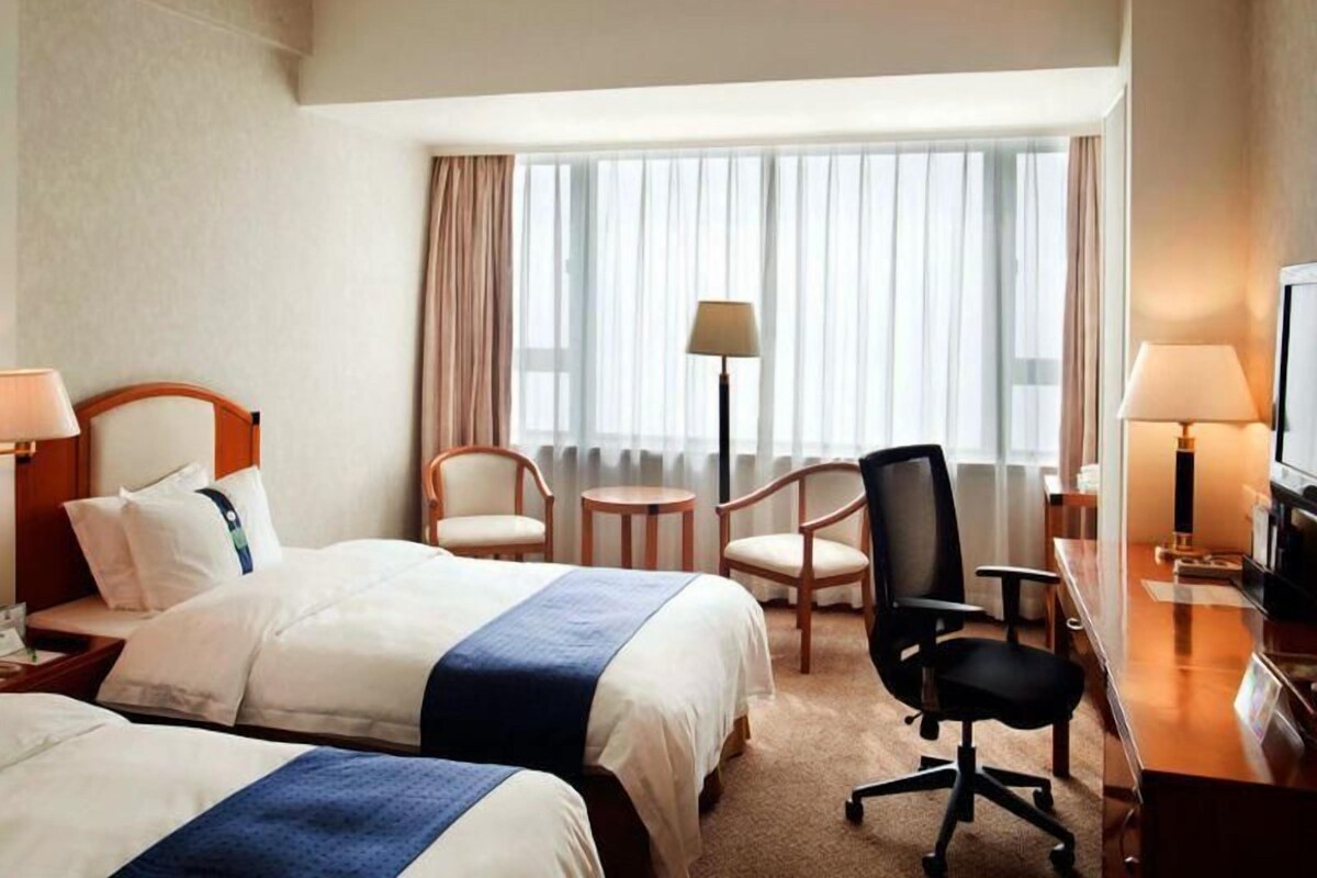 A hotel room with two beds, a desk, a chair, a television, and a window with curtains.