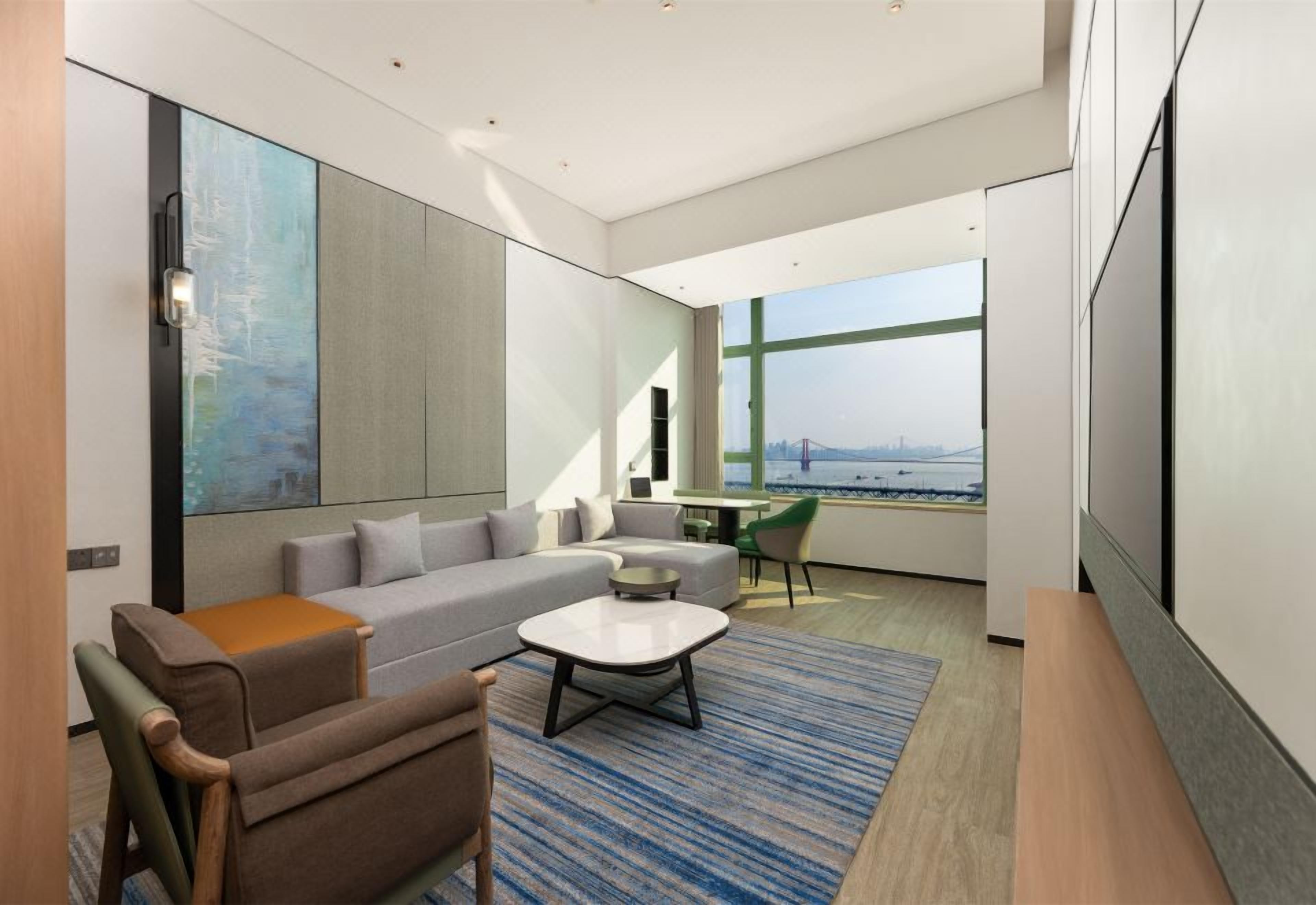 A modern living room with a sofa, coffee table, and a view of a cityscape through large windows.